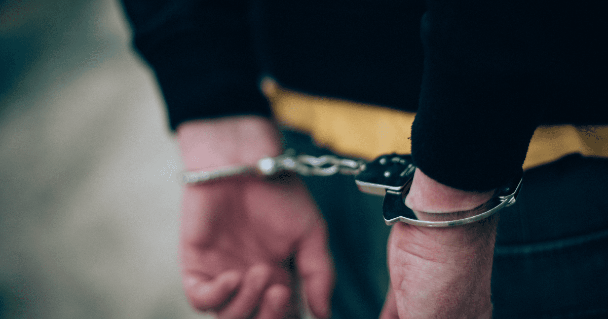 Arrest stock image of white man's hands in cuffs behind their back.