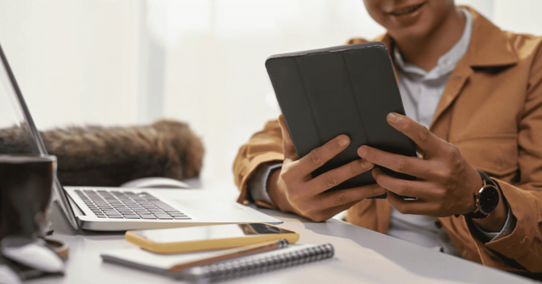 Man with ipad at desk with cat and coffee cup and laptop