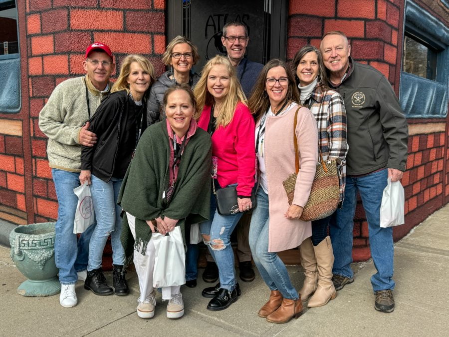A group of 9 friends pose for a picture in front of the Atlas Saloon during the Chocolate Tour in Downtown Excelsior Springs