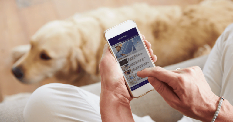 someone sitting on a chair with legs crossed holding a cell phone and looking at news daily with a golden lab at their feet