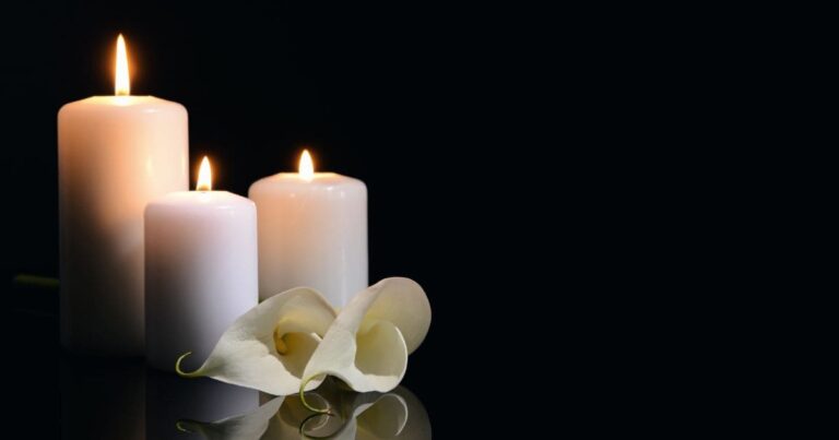 Three white candles burning with white flowers and a dark backdrop for funerals