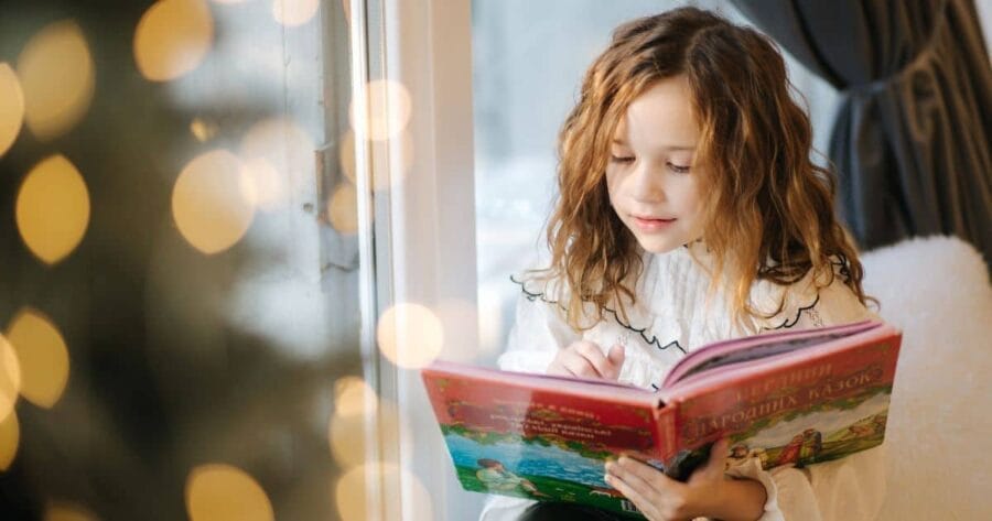 Winter library programs - young girl reading a book with a Christmas tree blurred in the foreground